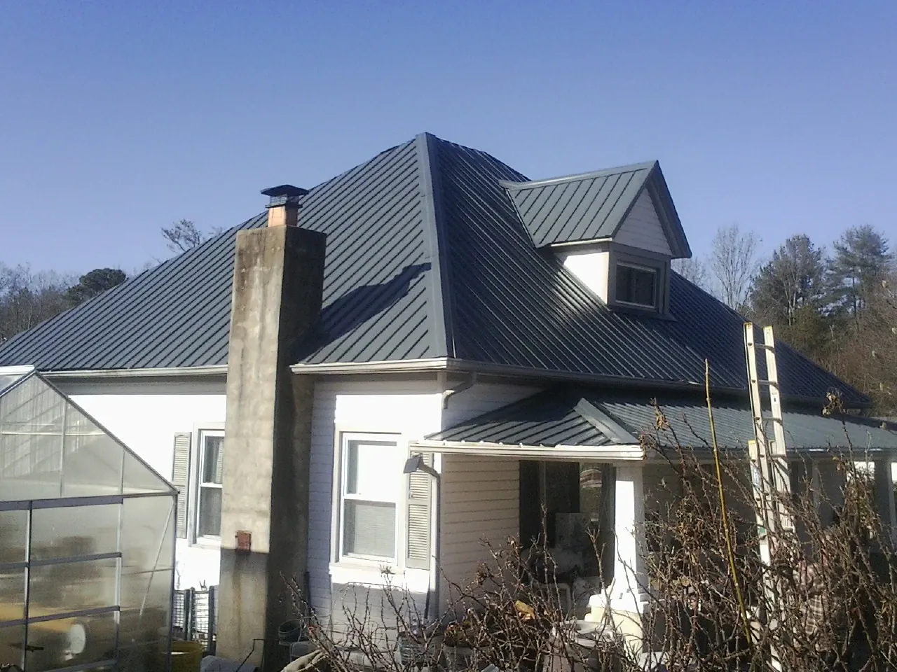 Dark blue standing seam metal roof on a white farmhouse with dormer — Slate & Tile Roof Repair by Roofing Brothers in Geneva