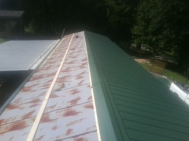 Old rusted panels beside newly installed green metal roofing — Wind Damage Roof Repair by Roofing Brothers in Geneva