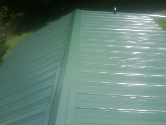 New green metal panels meeting at the ridge of a roof — Flat Roof Repair work by our crew in Geneva
