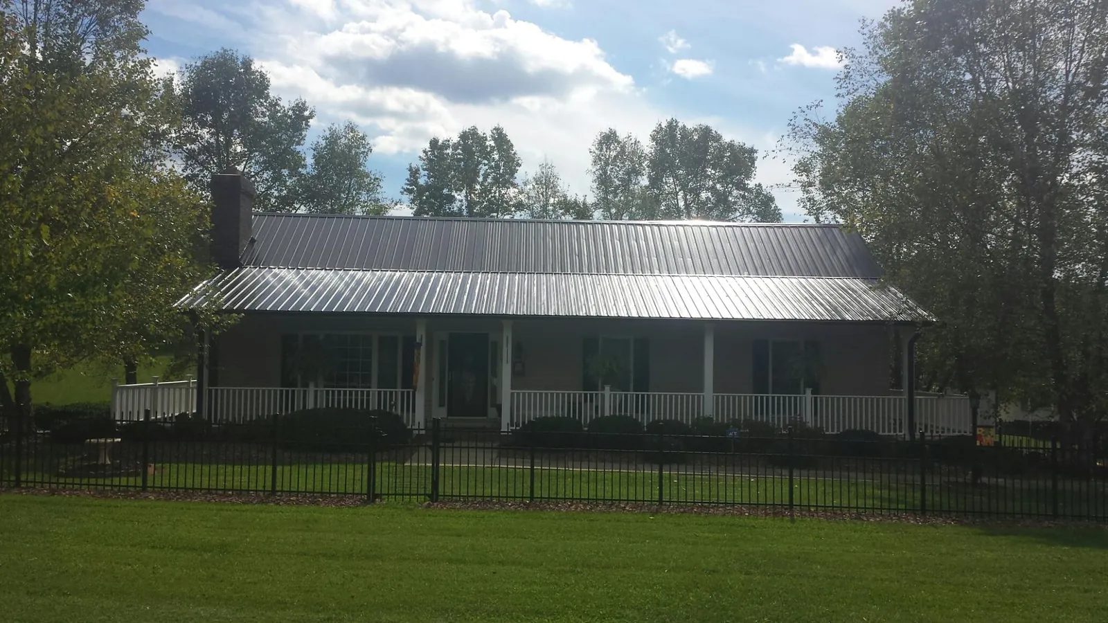 Gray metal roof on a brick ranch with a full width front porch — Gutter Guard Installation work by our crew in Geneva