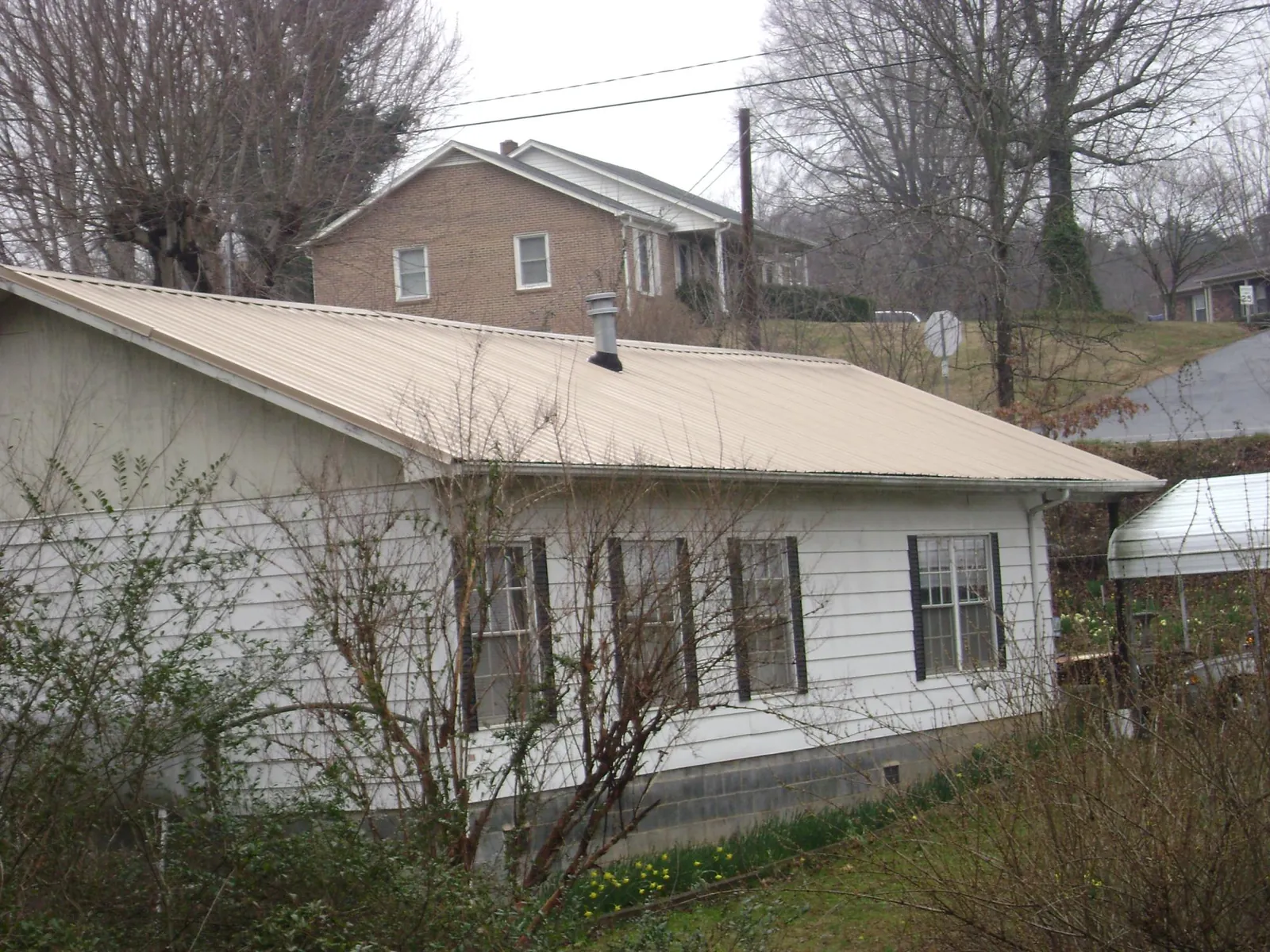 Tan metal roof on a white sided house set into a hillside — Commercial Roofing by Roofing Brothers in Geneva